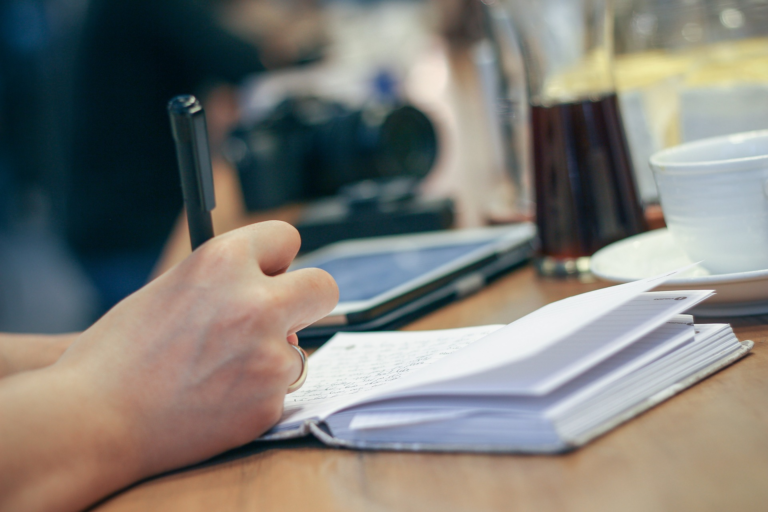 Person writing in notebook beside coffee cup